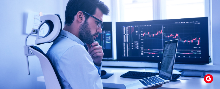 A man sits in front of a laptop displaying stock market graphs, focused on day trading activities.