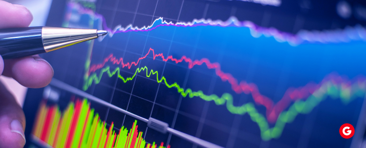 A person holds a pen, pointing at a stock chart displayed on a screen, indicating data trends and analysis.