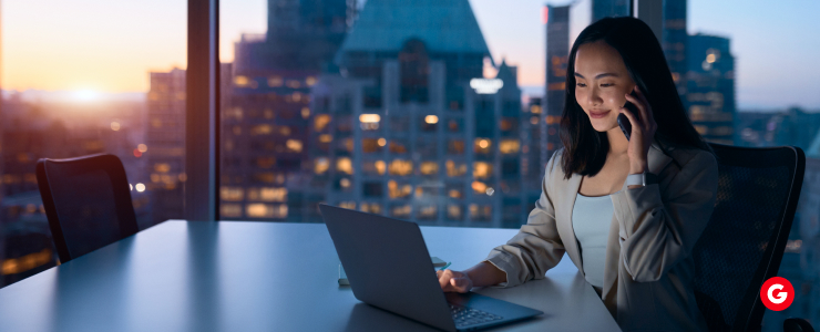 A woman sitting at a desk, using a laptop while talking on the phone.